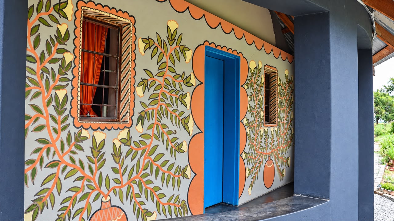 A hand-painted mural of leaves and flowers decorating the wall of a Shayanewako building, with a bright blue door